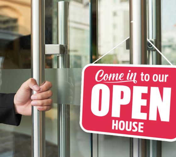 Glass doors with hand on one handle and sign hanging that says Come in to our OPEN HOUSE