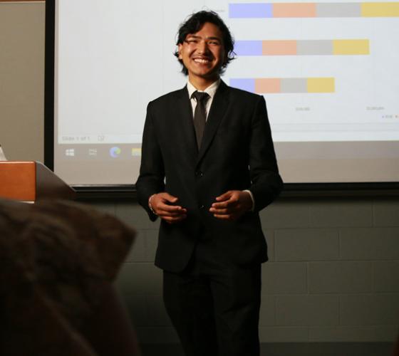Business student smiling during presentation with screen behind him