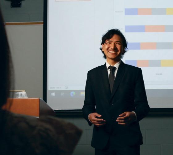 Business student at front of class doing a presentation smiling at camera and class
