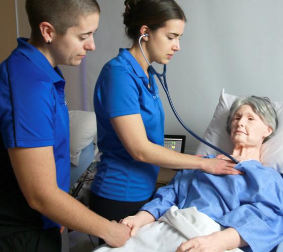 Two nursing students checking vitals and supporting mannequin patient in simulation lab