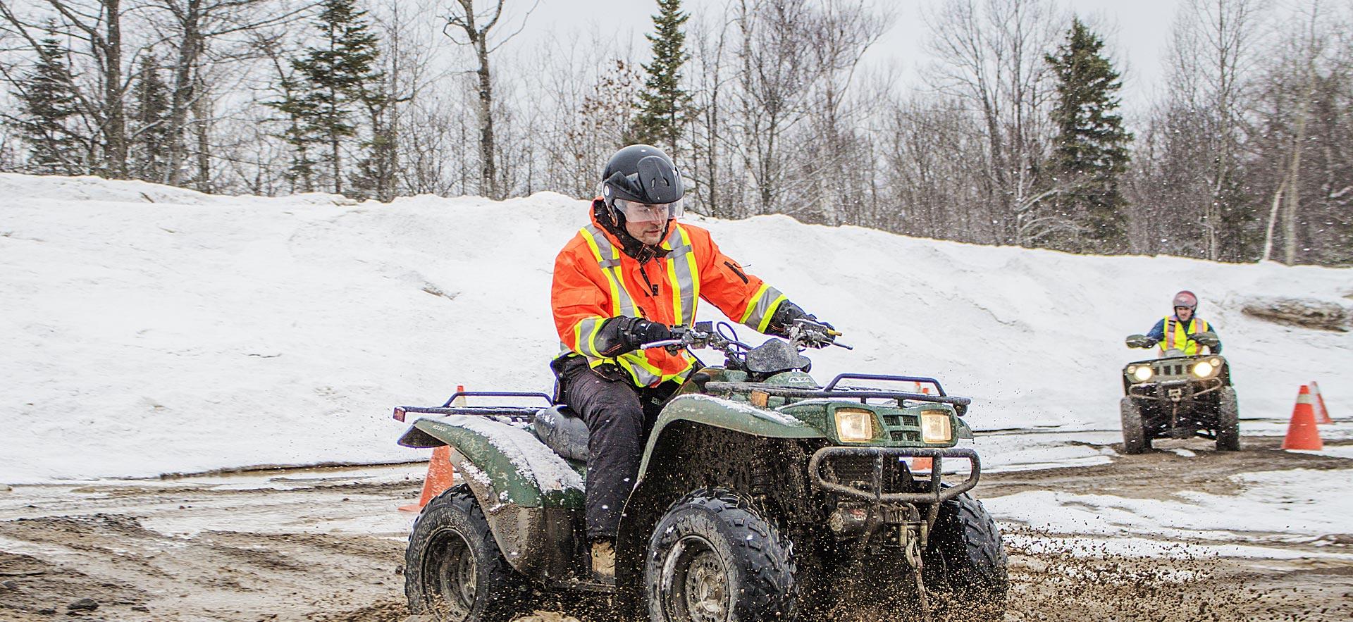 A male Adventure Recreation and Parks Technician student dives an ATV 4-wheeler though snow and slush. 