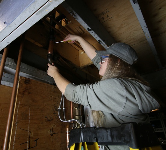 Plumbing student from women in trades program working with pipes on a ladder