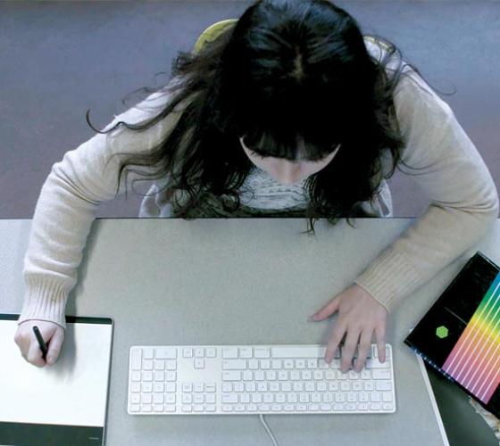 A female Graphic Design - Digital Media student works at her computer in class.