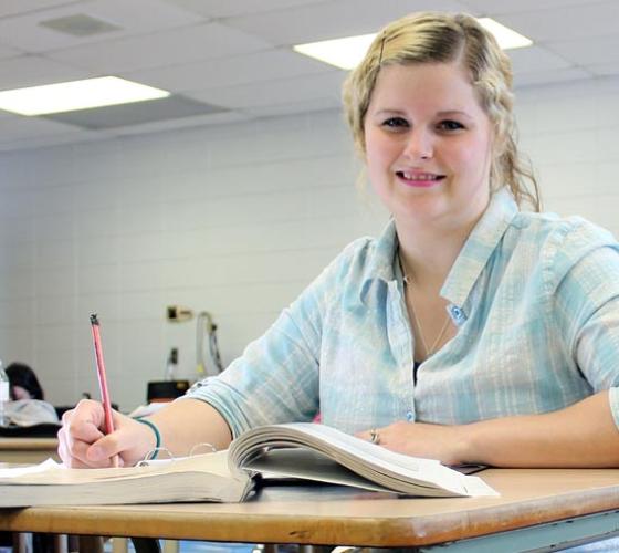 One female Academic Upgrading student smiles while sitting at her desk in class.