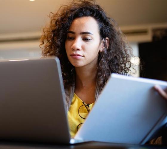 Young woman reading information on a computer and book.