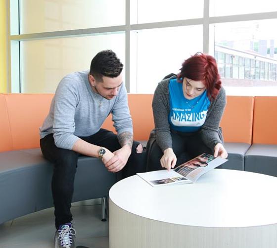 Male student reading through Sault College view book with female recruiter.