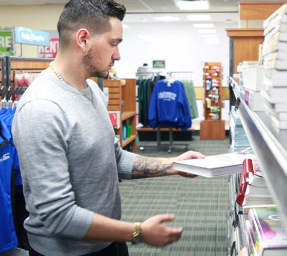 Male student reviewing a book in the book store.