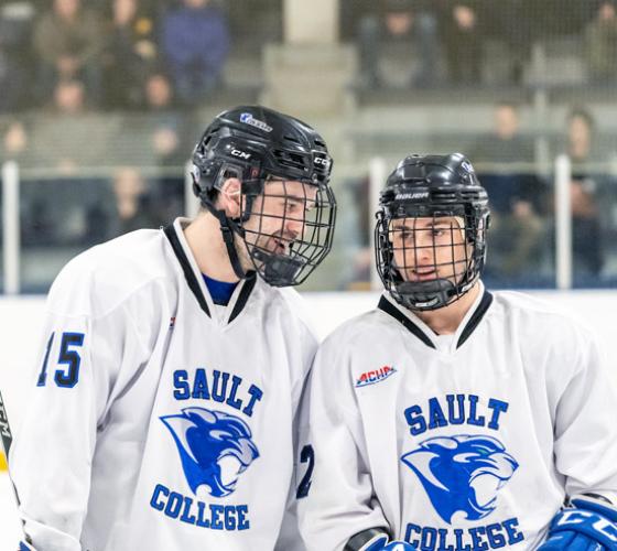 Two male cougar hockey players stop and talk.