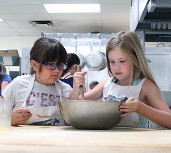 Two young girls mixing cake batter in a bowl.