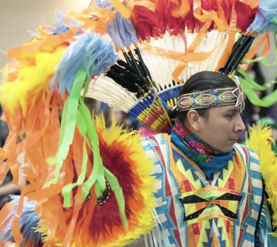 Wearing a colourful costume, an indigenous male dances at a pow wow.