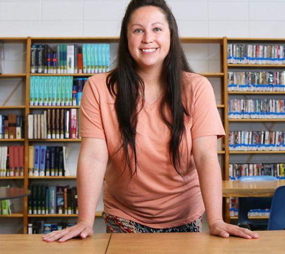 student standing and smiling in front of bookshelf