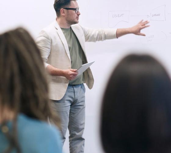 male making presentation at whiteboard for small group of people