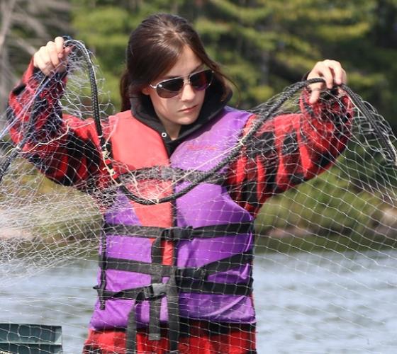 student wearing lifejacket and organizing net while on a boat in the water