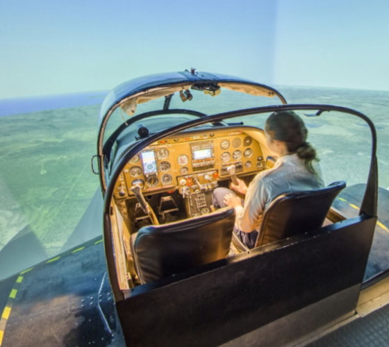 female student sitting using the aviation simulator with large screen in background showing sky in flight