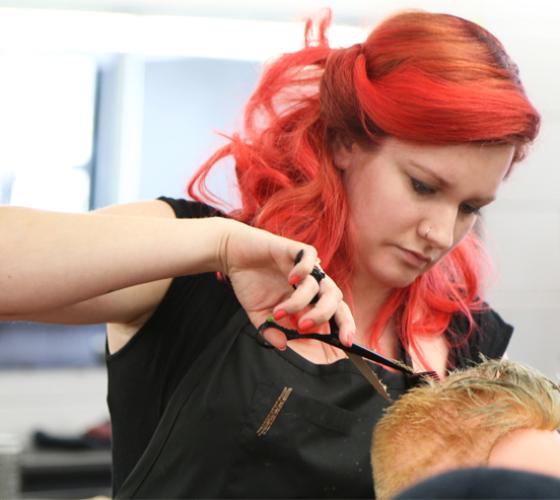 hairstyling student standing behind client seated while trimming hair with scissors in salon