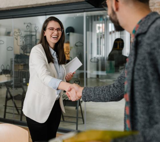 woman smiling shaking hands with man in a office with a large window wall