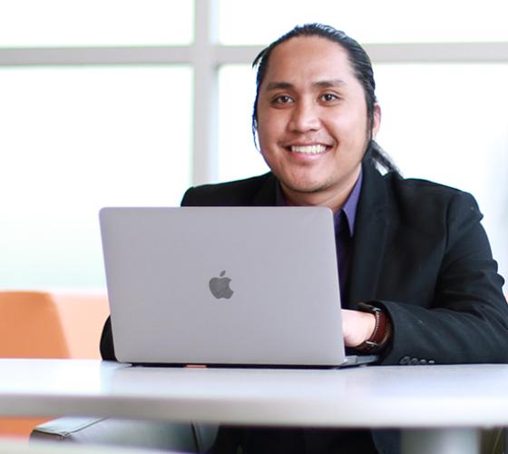 Paul a student of our Business - Accounting program smiling at camera sitting with laptop