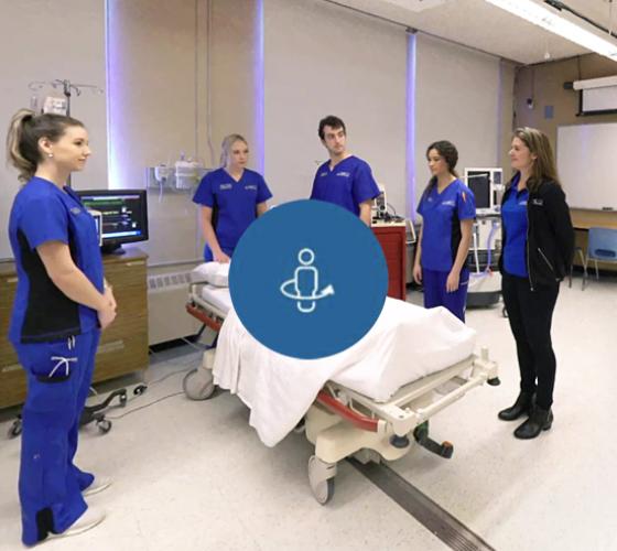 Nursing students with instructor around bed with mannequin in simulation lab for virtual tour