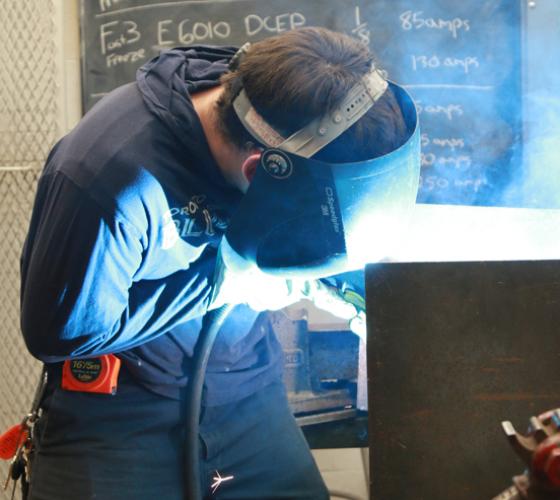 Trades student in coverall wearing welding mask for his work