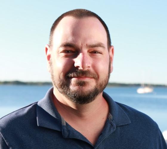 Chris a graduate of our Electrical Engineering Technology program smiling with waterfront in background