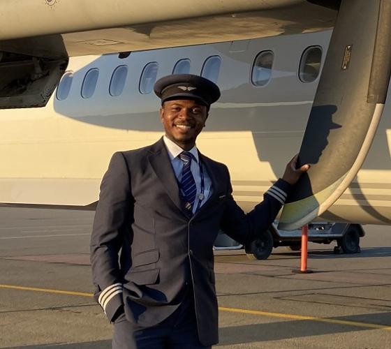 George smiling at camera beside plane holding propeller