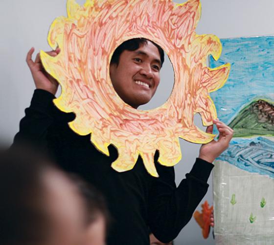 ECE student smiling and holding up paper sun while interacting with children