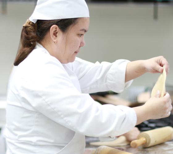 Culinary student in kitchen rolling out dough