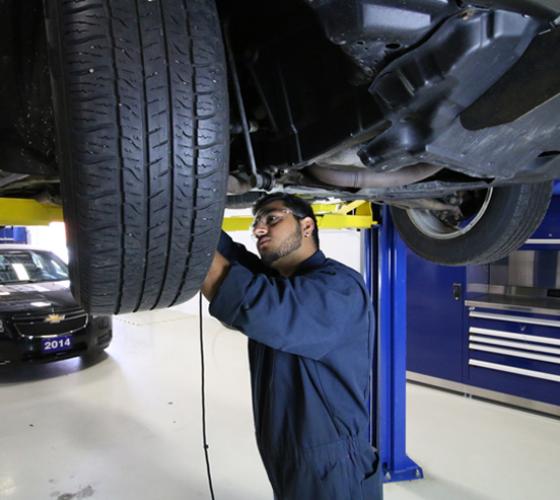 Automotive student in coverall working in the Motive Power Centre under vehicle lift