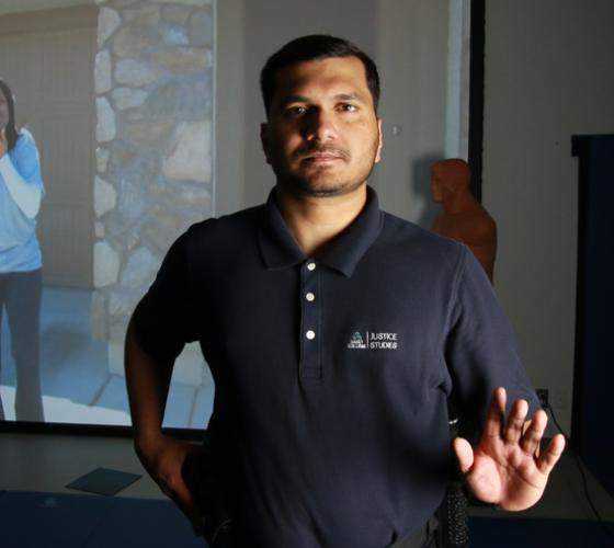 Policing student in uniform looking at camera with MILO simulation training on screen in background