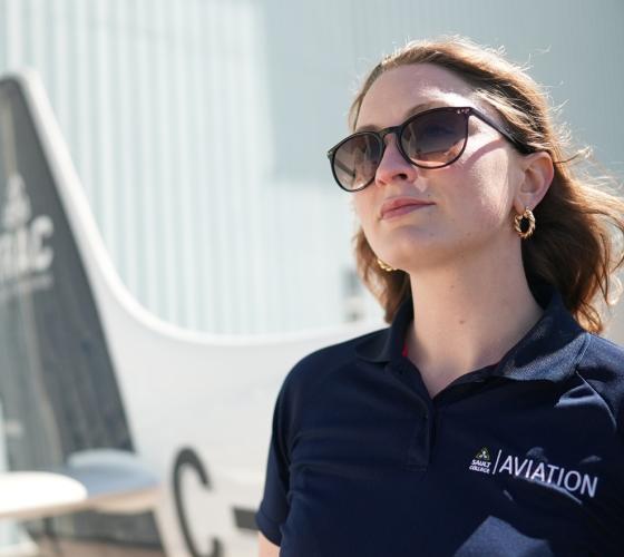 Aviation student Amanda looking up at the sky standing in front of a plane
