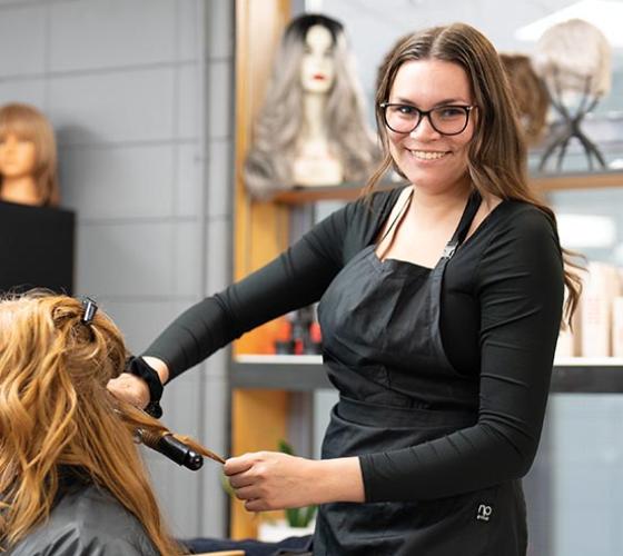 Hairstyling student styling client's hair and smiling at the camera