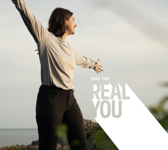 Student with arms spread out smiling looking out from a hill