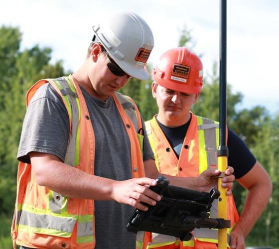 Engineering student in hard hat and vest on construction site with employer