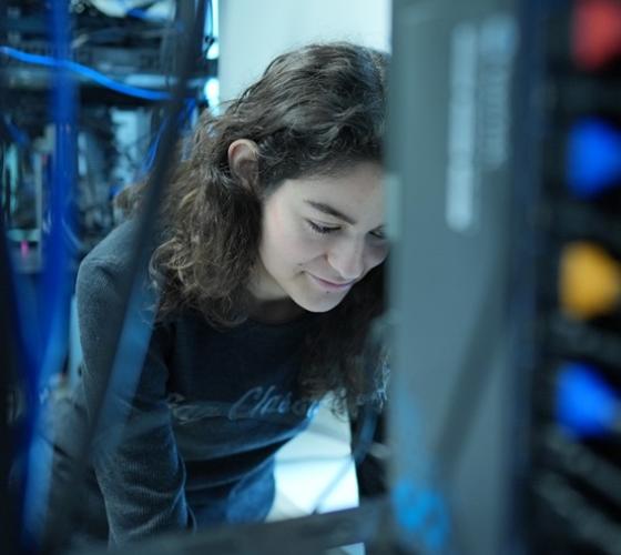 IT student standing at networking stacks leaning over typing on keyboard