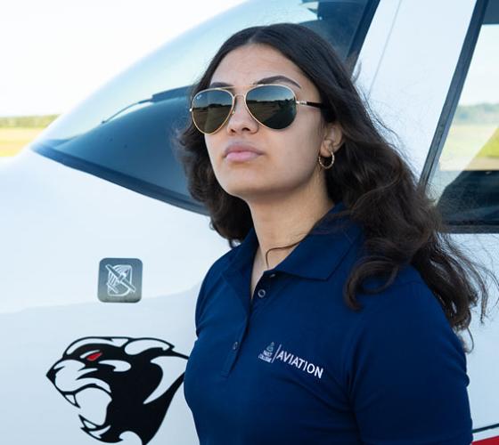 Aviation student with sunglasses on standing in front of plane at Hangar