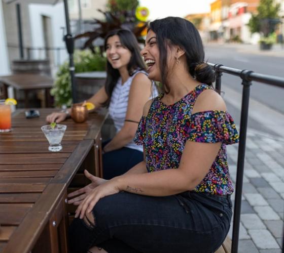 Two young women laughing on patio downtown in summer having drinks