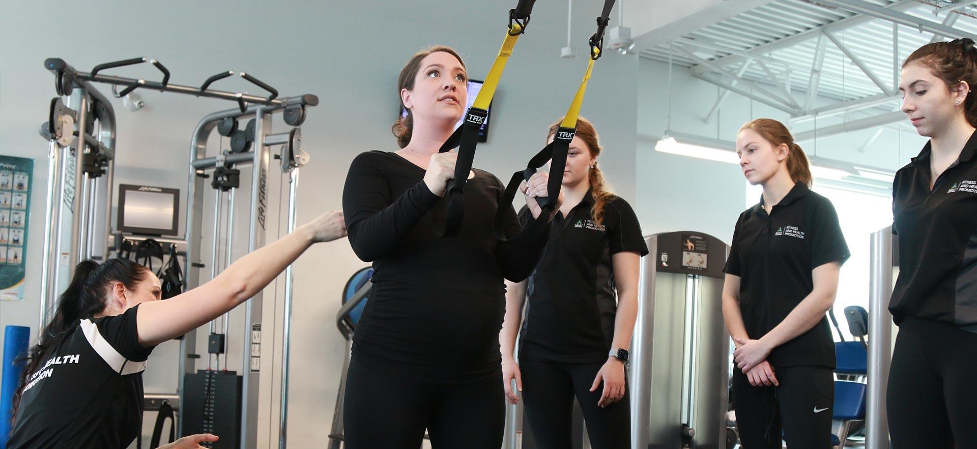 An expectant mother is shown proper exercise techniques in front of fitness and health students.