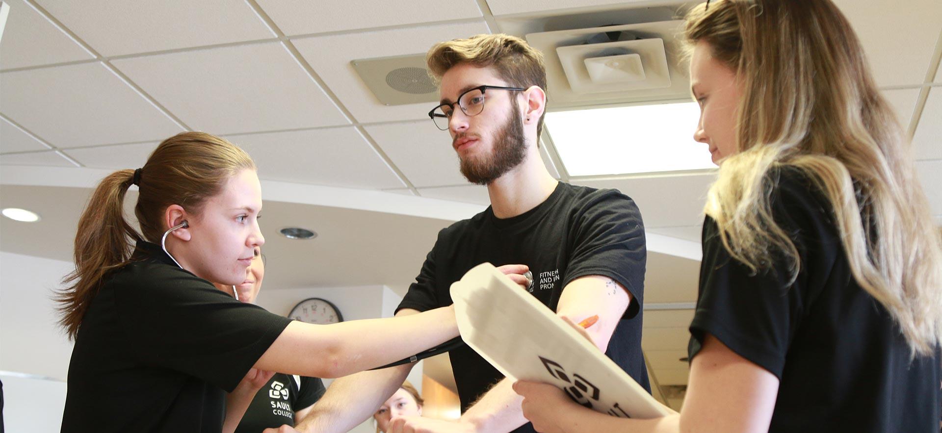 A male fitness and health student gets his heart rate checked by other students.