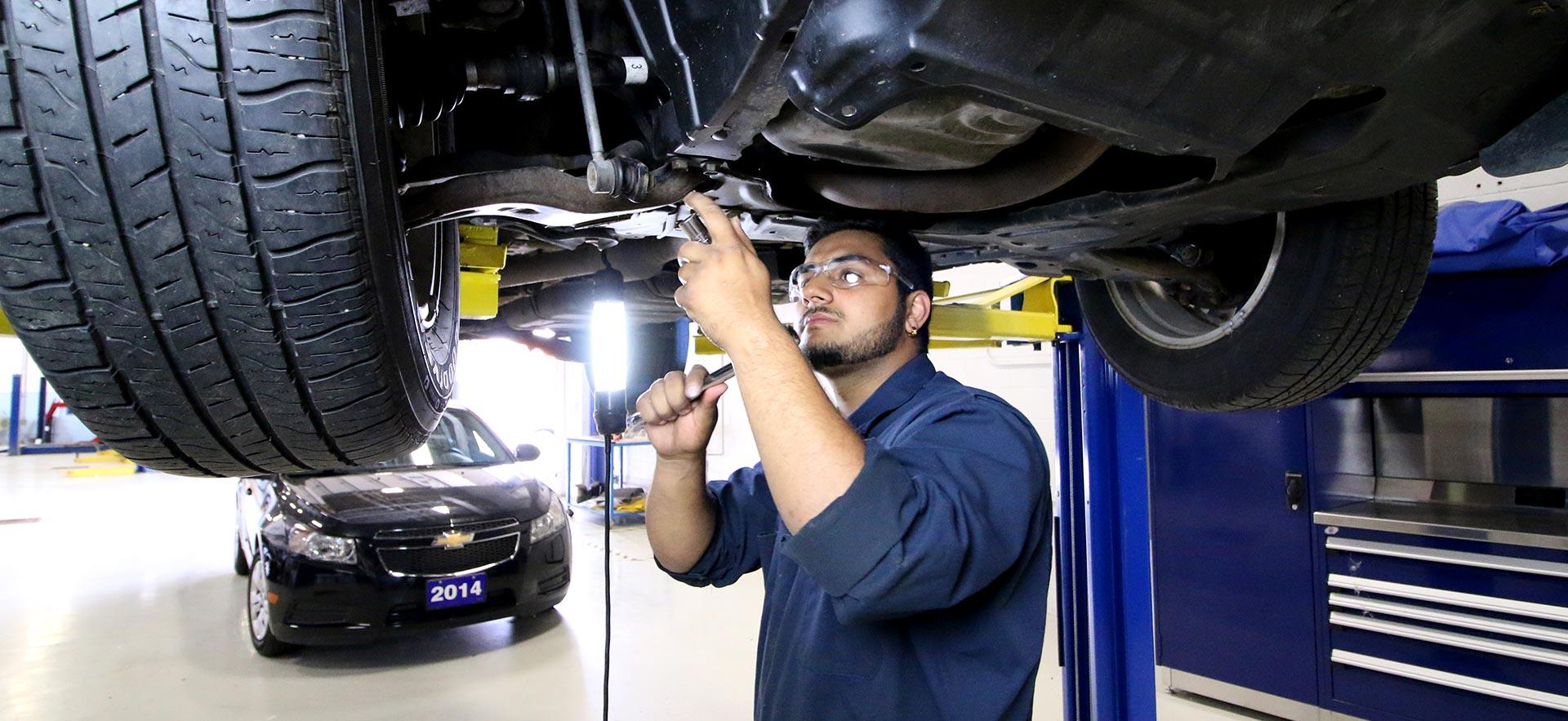 One male Automotive Service Technician student works on a car on a hoist.                                                                 