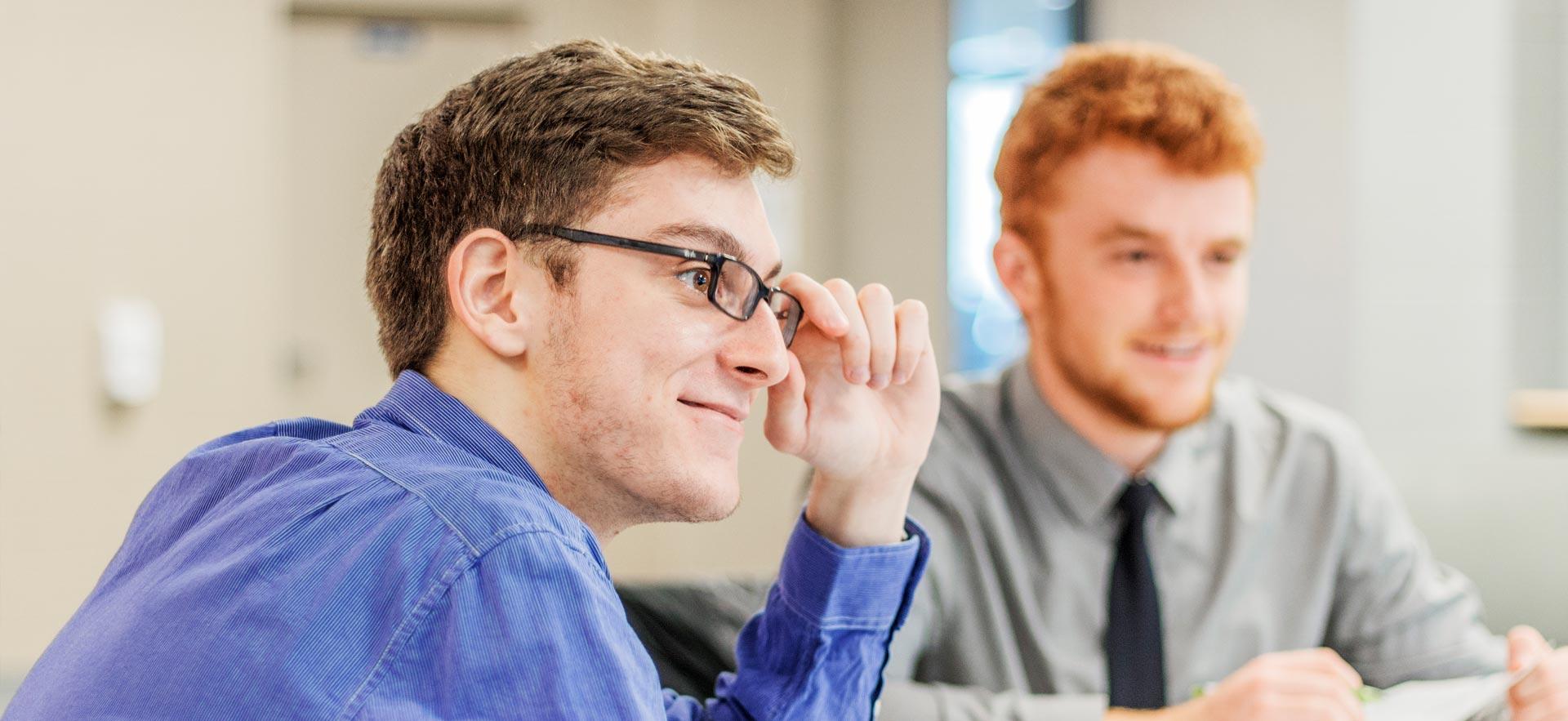 Sault College business student smiles and touches his glasses as he listens to his instructor. 
