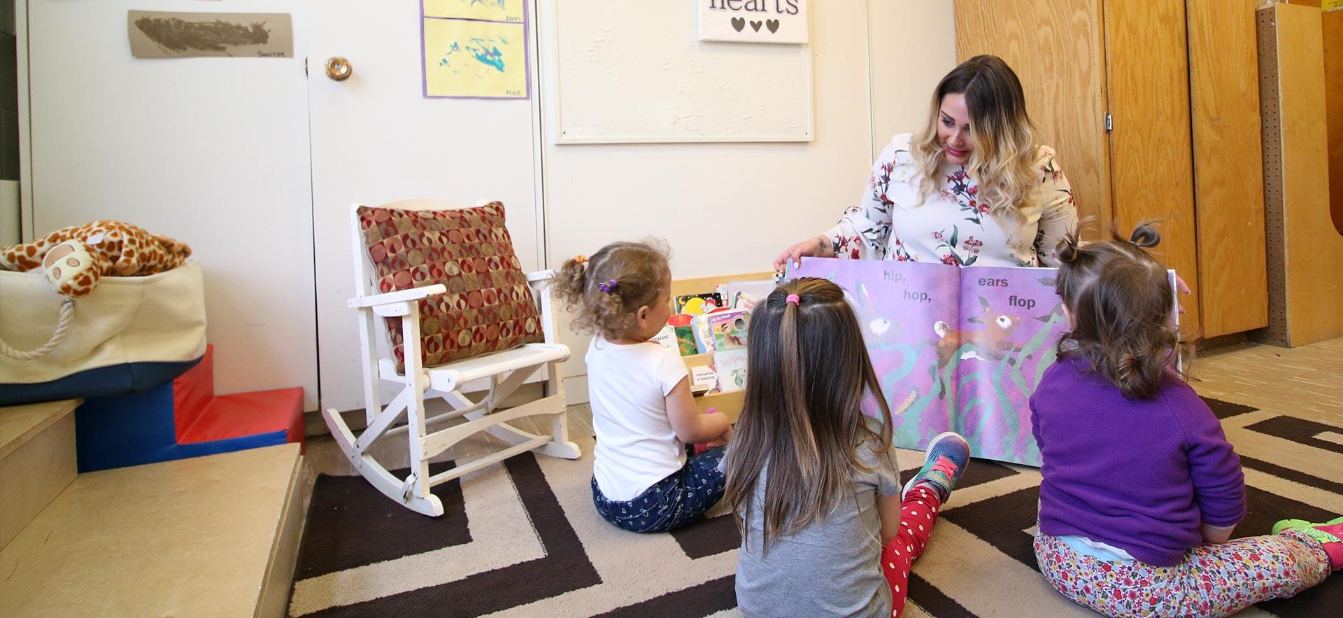 One female Early Childhood Education student reads a story book to some young children. 
