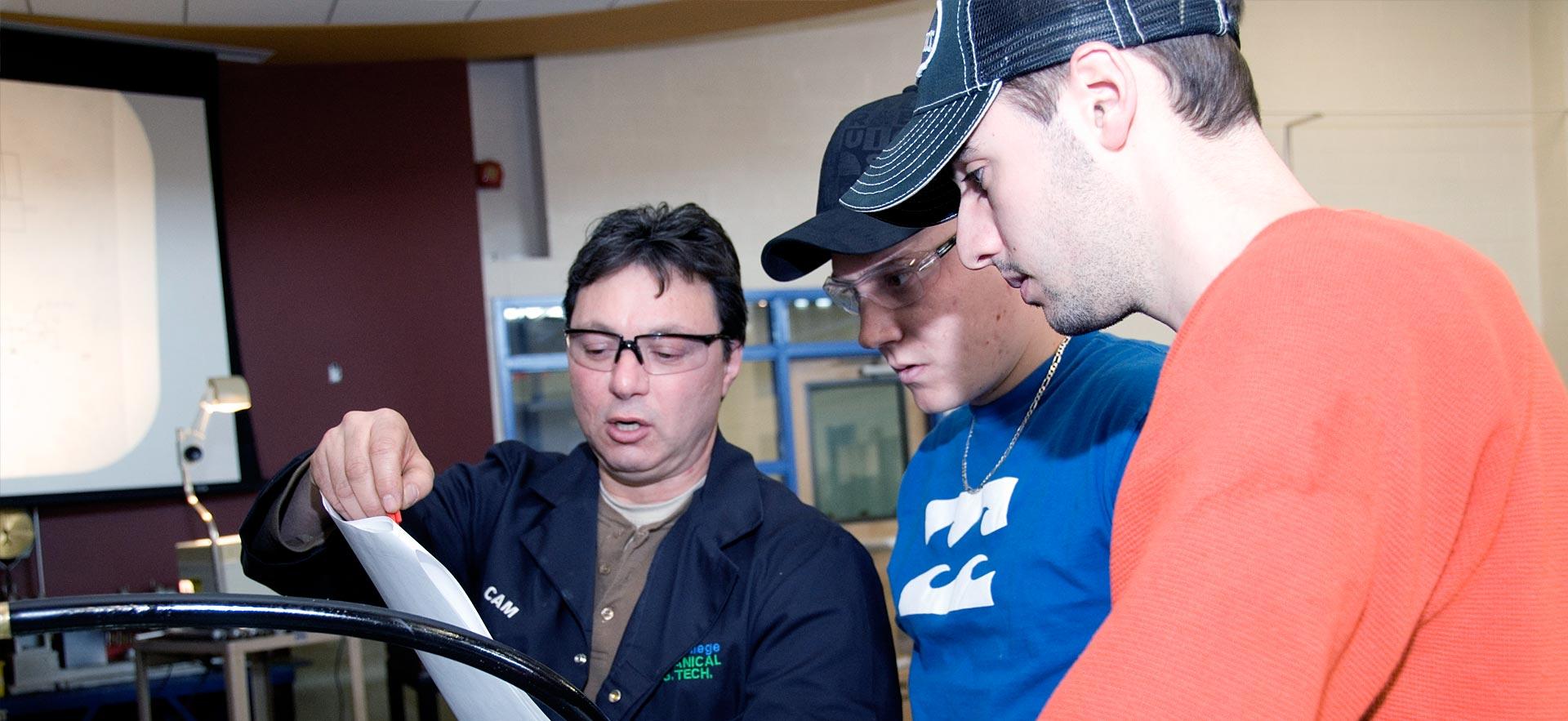 Two male Mechanical Engineering Technology students listen to their instructor explain a lesson. 