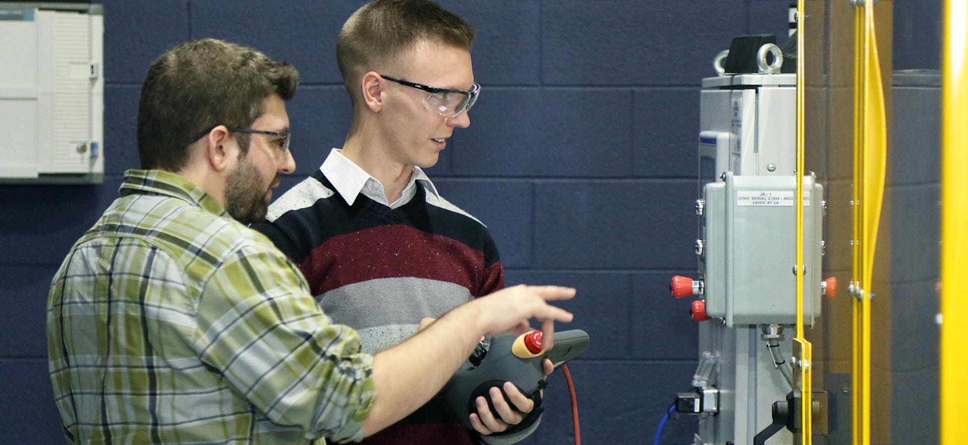 Two male Automated Manufacturing students demonstrate their automated class project. 