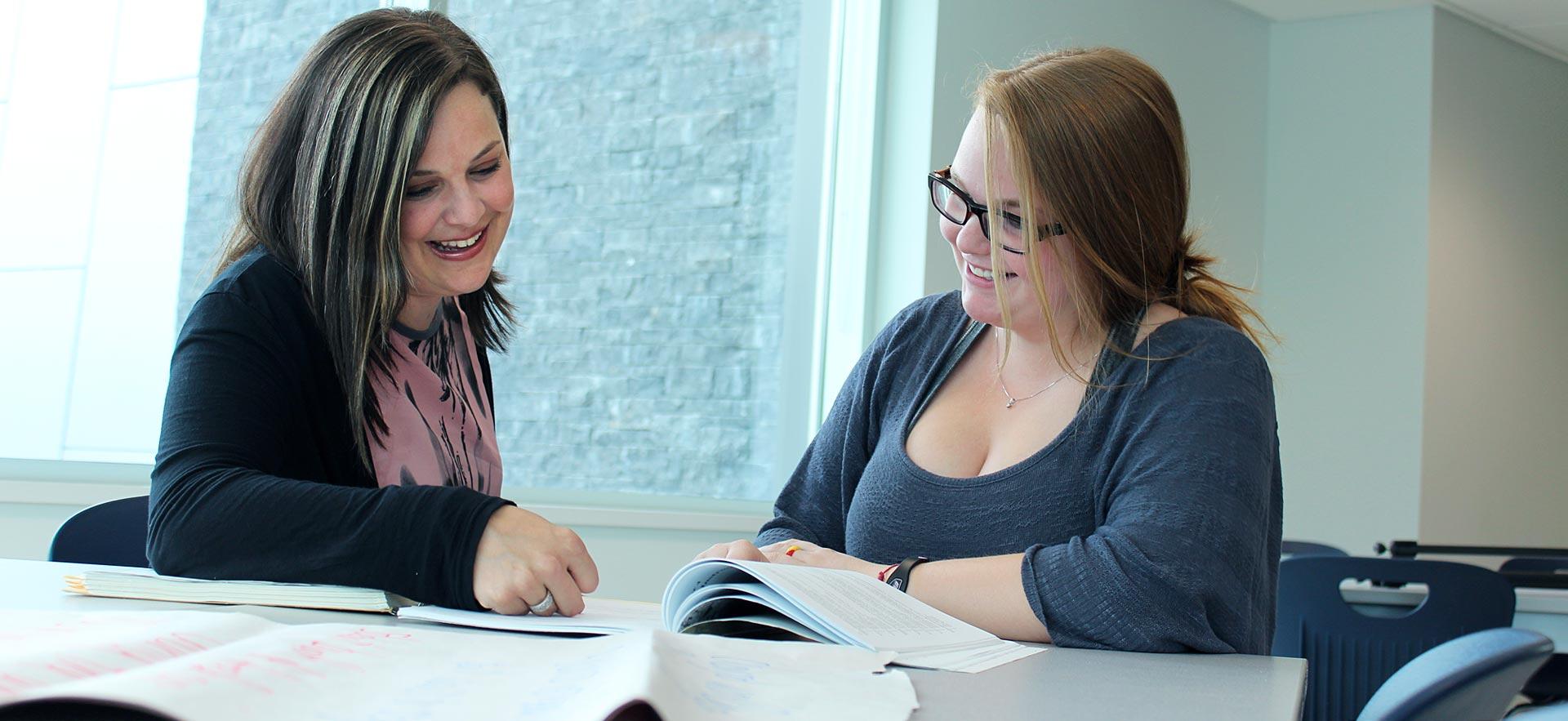 One female General Arts and Science student smile and laughs with her instructor during class.