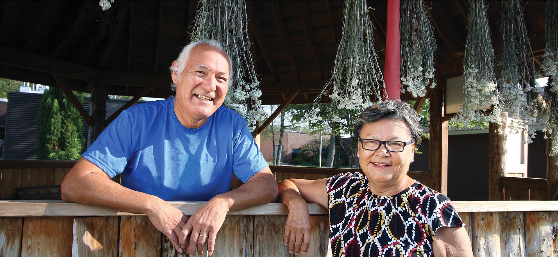 Male and female Sault College Indigenous Elders smile for a photo.