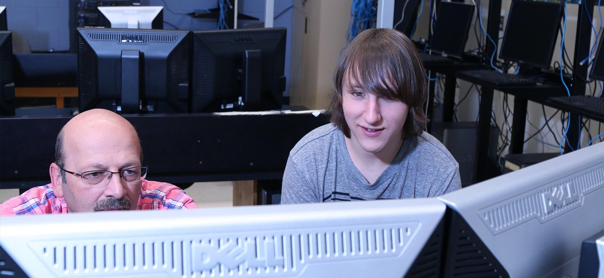 One male Computer Programmer student observes a computer screen of code while listening to his instructor. 