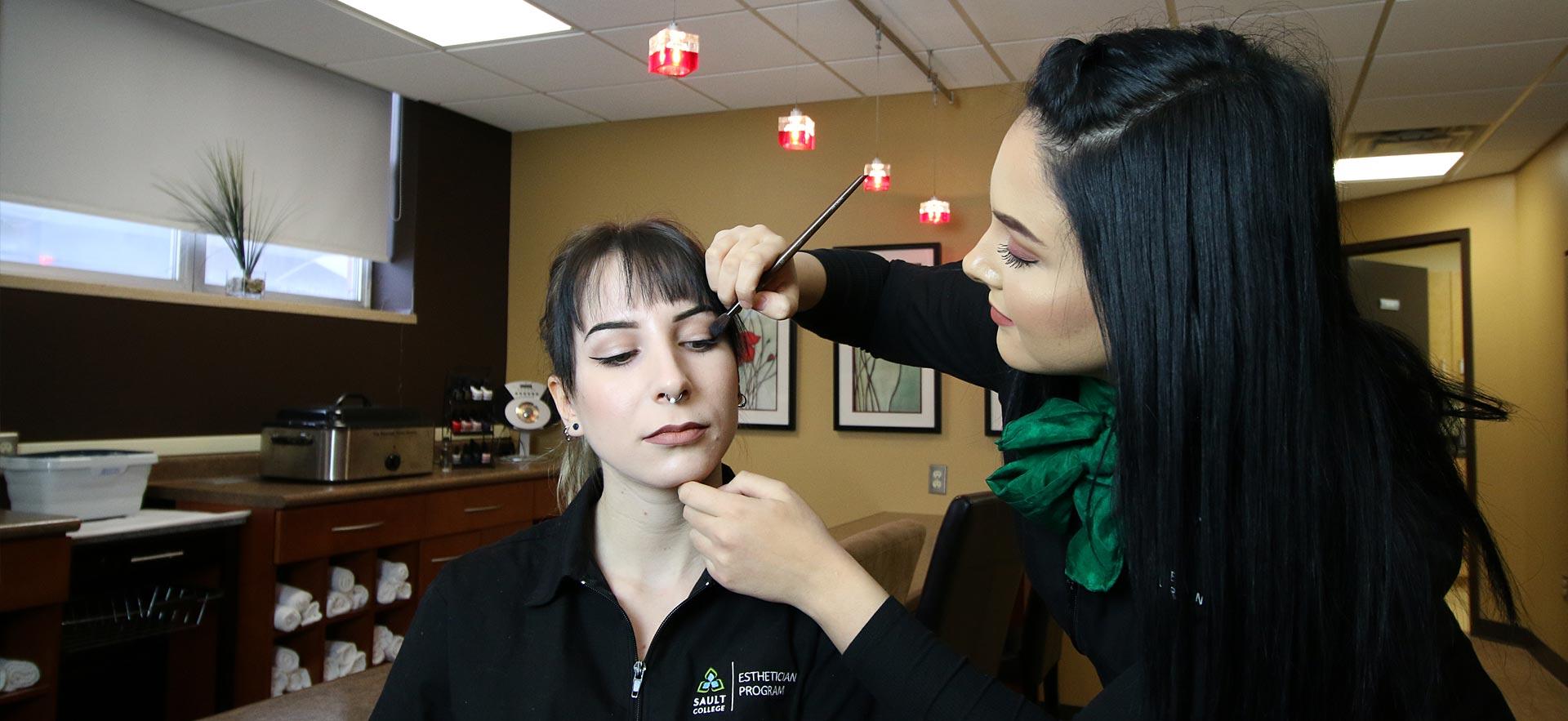 One female Esthetician student applies make-up to another Esthetician student in the Sault College salon spa. 