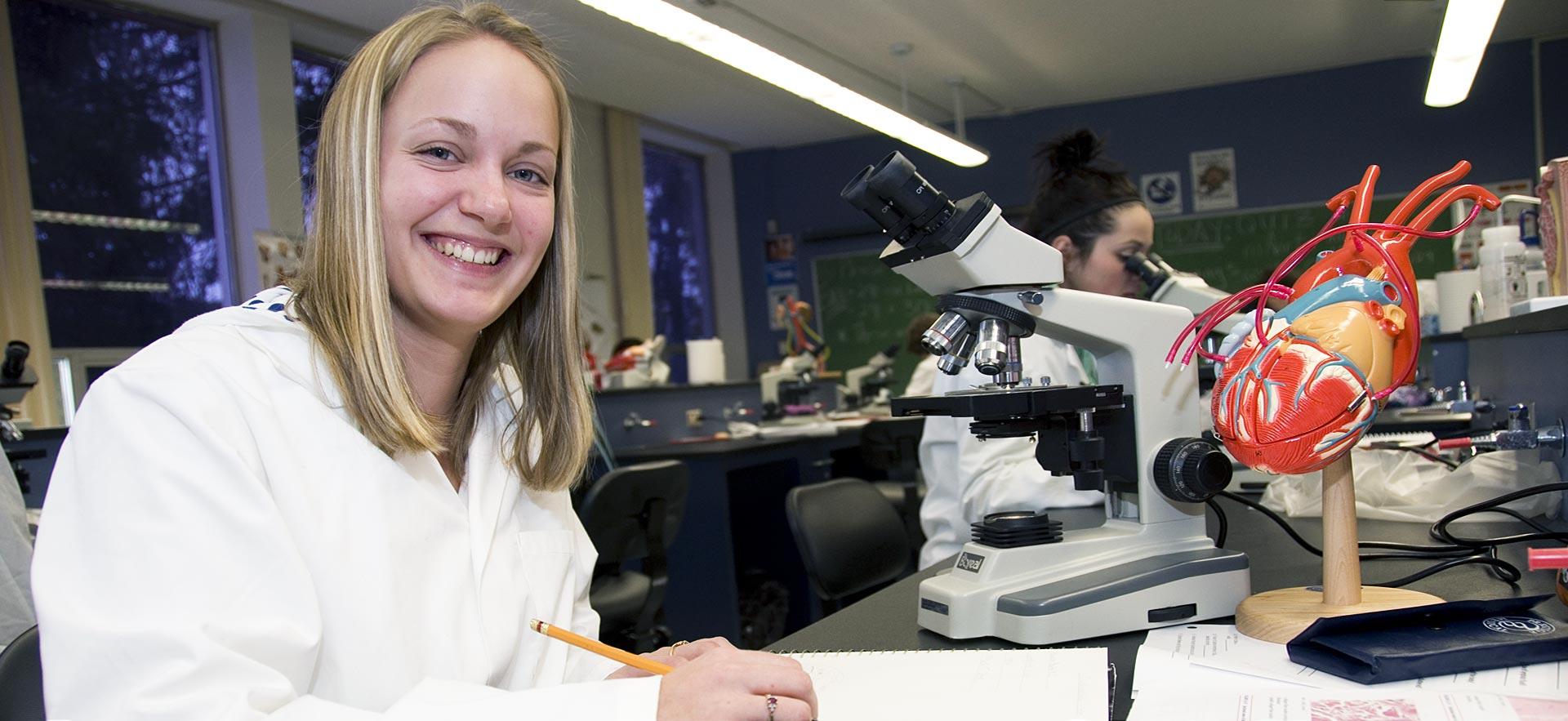 Female nursing student smiles while working on a lab assignment.
