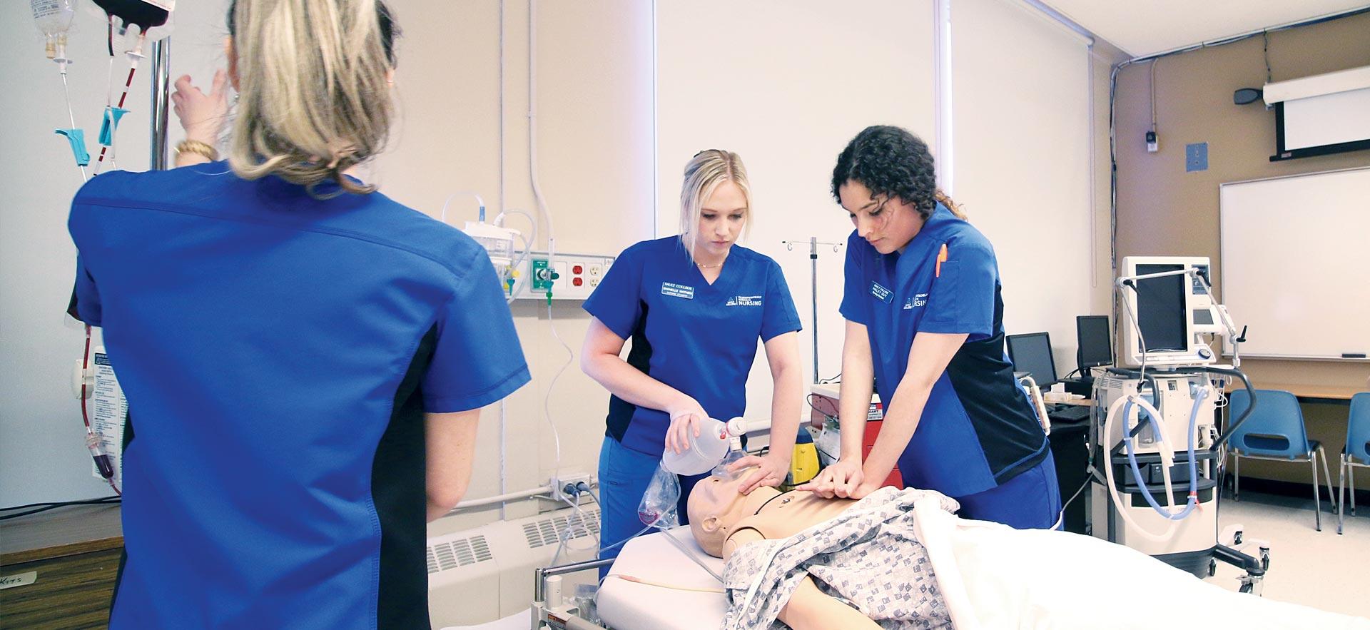 Female nursing students practice reviving a medical mannequin.