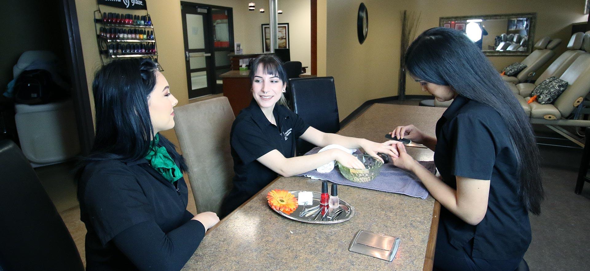 Female esthetician student applies a finger nail treatment to a fellow student.